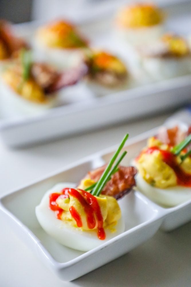 picture of deviled eggs with sriracha, bacon, and chives on a white plate