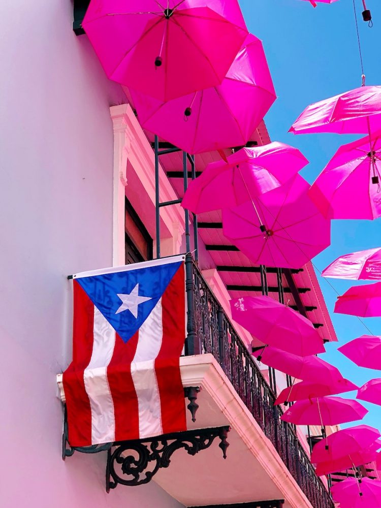 picture of pink umbrellas hanging off a building and a Puerto Rico flag hanging off a balcony