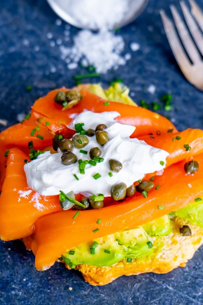 piece of bread with avocado, salmon, creamy, capers, and chives on it