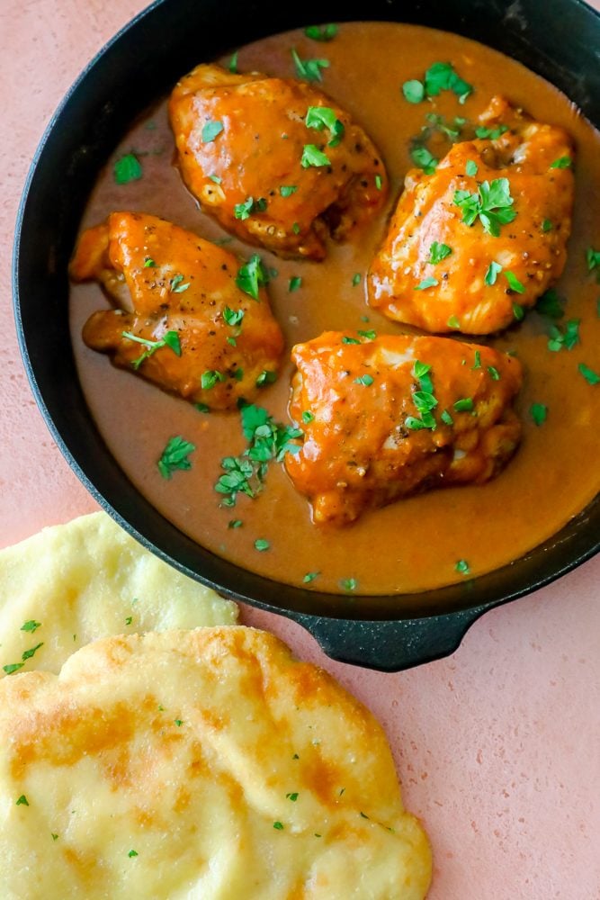 naan bread next to a pan of butter chicken on a pink table