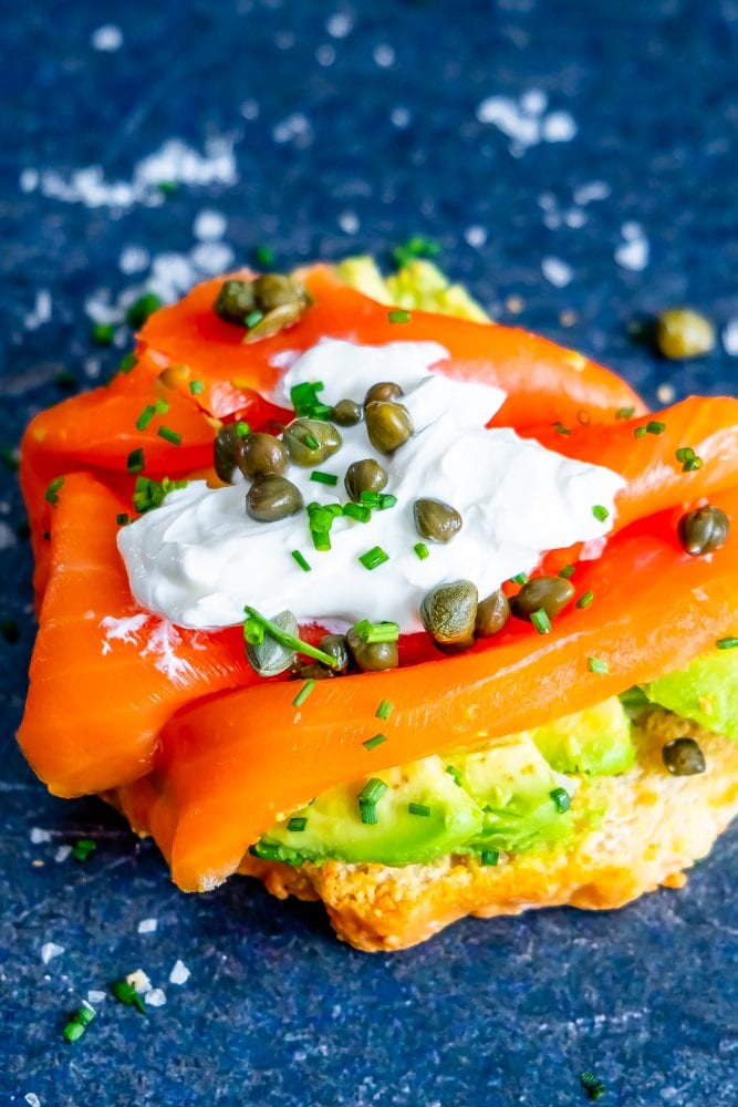 piece of bread with avocado, salmon, creamy, capers, and chives on it