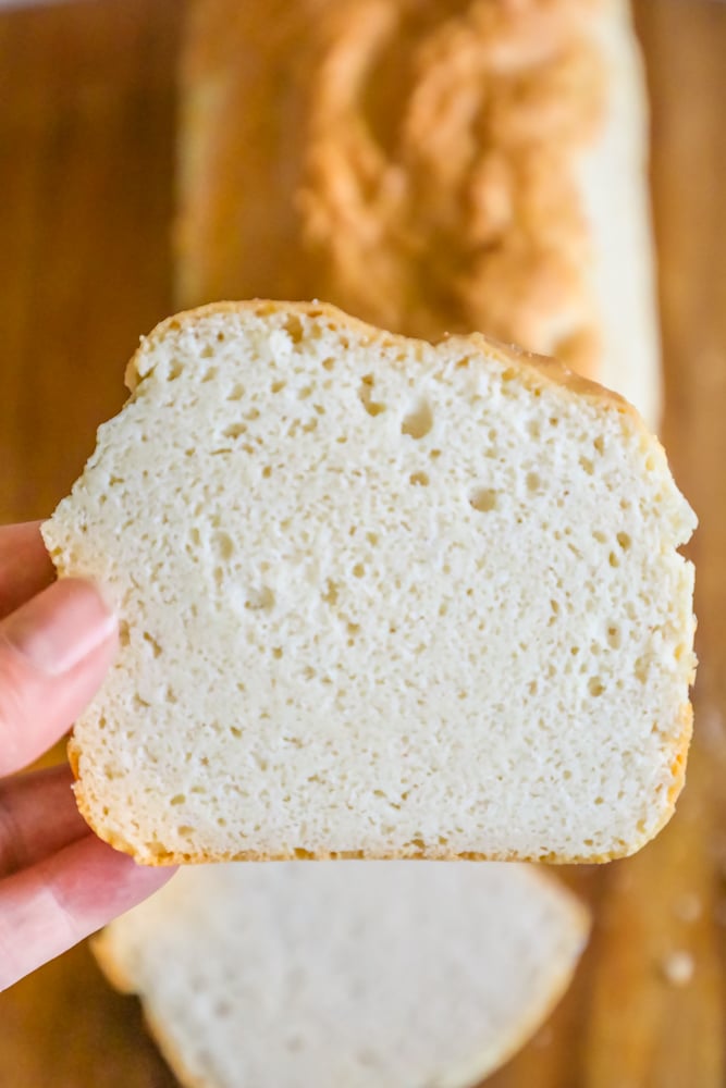 A person showcasing the Easy Keto Sandwich Bread Recipe by holding a slice of bread on a cutting board.