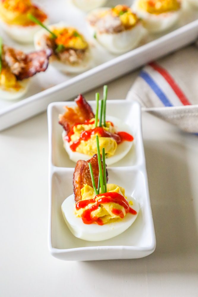 picture of deviled eggs with sriracha, bacon, and chives on a white plate