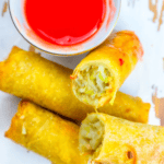 Plate of crispy homemade egg rolls with a side of red dipping sauce.