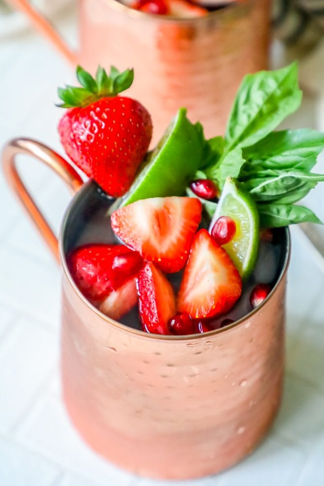 picture of moscow mule in a copper cup with strawberries, mint, basil, and ice in it