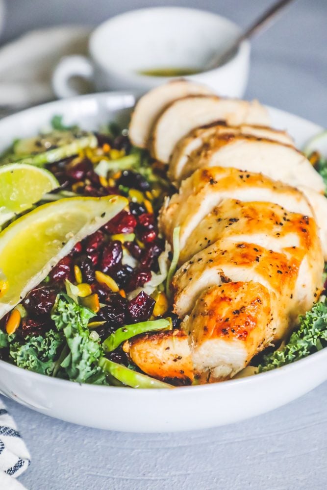 salad with nuts, kale, cranberries, poppyseeds, lemon, lime, and roast chicken in a white bowl