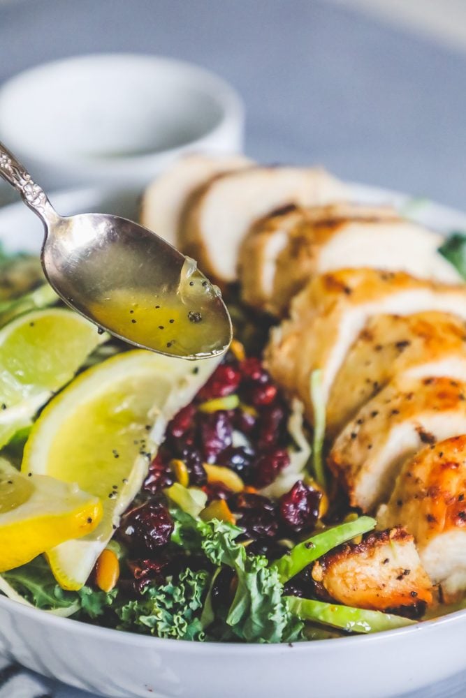 salad with nuts, kale, cranberries, poppyseeds, lemon, lime, and roast chicken in a white bowl