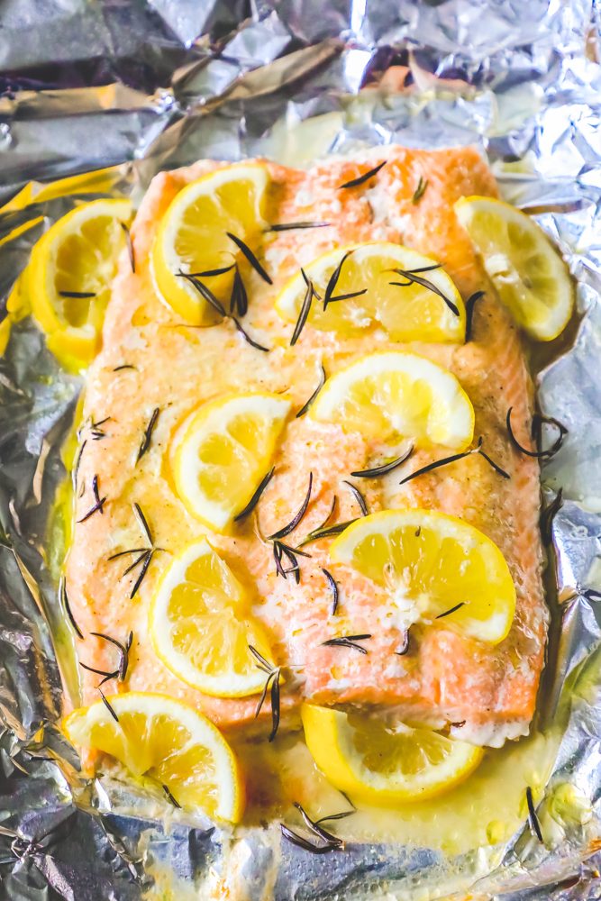 baked salmon filet on a baking sheet lined with foil topped with butter, rosemary, and lemon slices