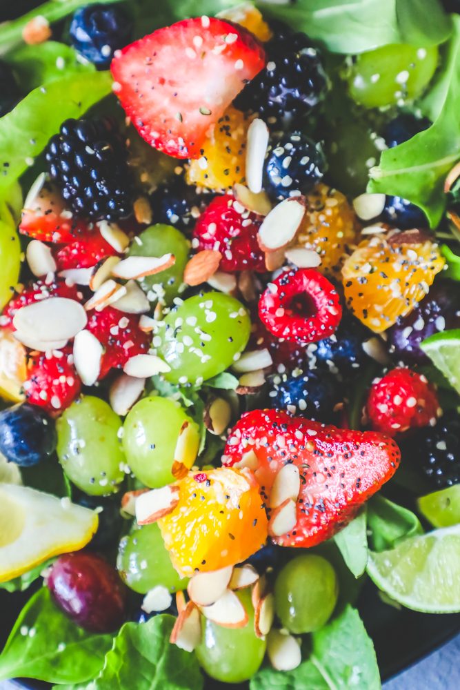 fruit salad with grapes, oranges, lemon, almonds, poppyseeds, strawberries, and lettuce in a bowl 