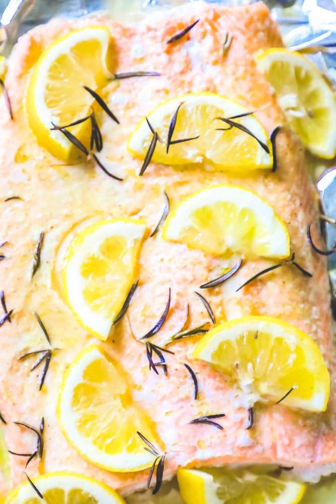 baked salmon filet on a baking sheet with slices of lemon, butter, and rosemary 