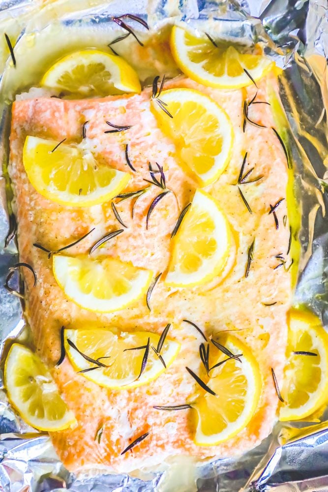 baked salmon filet on a baking sheet lined with foil topped with butter, rosemary, and lemon slices