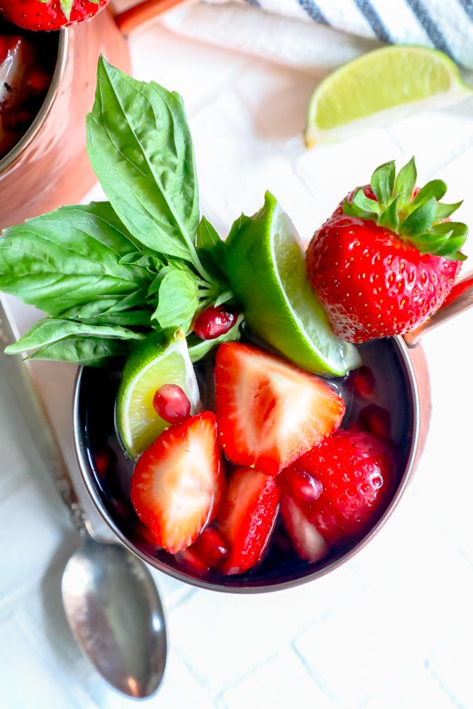 picture of moscow mule in a copper cup with strawberries, mint, basil, and ice in it