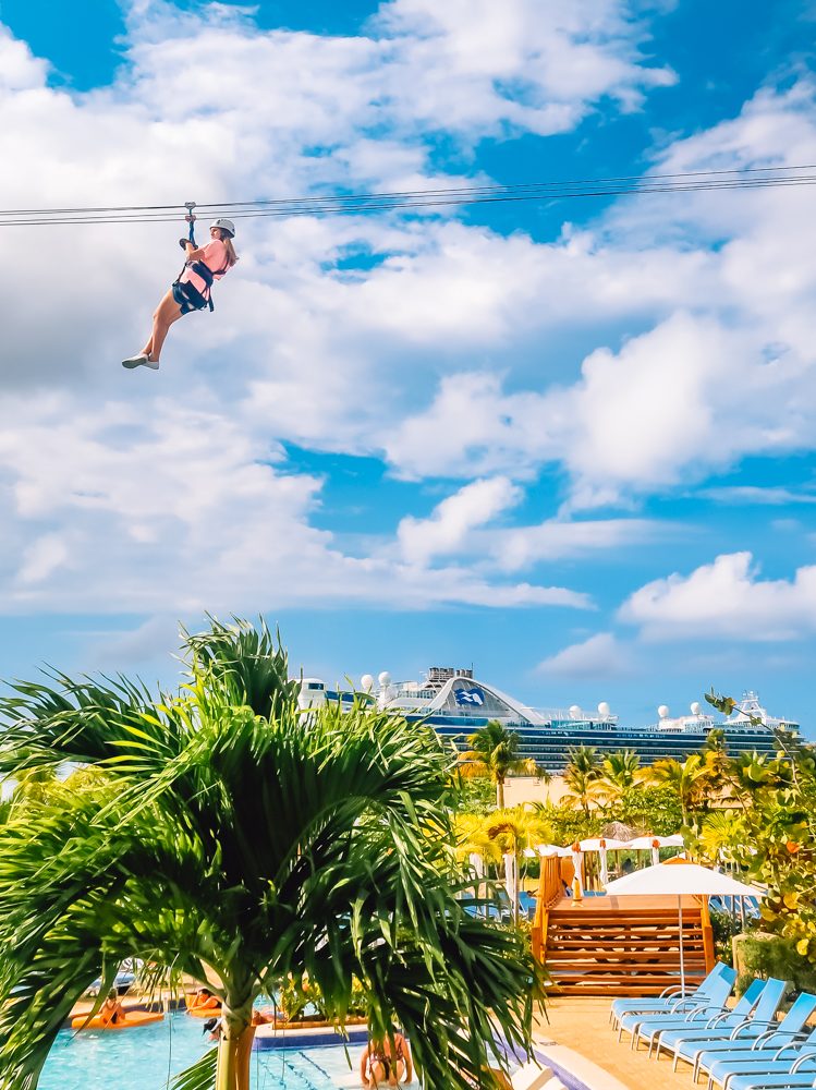 person ziplining with pool and cruise ship in the background, palm trees
