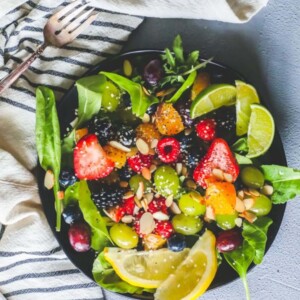 A bowl of fruit salad with almonds, lemons, and spinach.