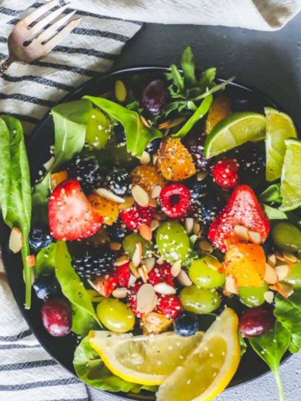 A bowl of fruit salad with almonds, lemons, and spinach.