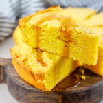 A slice of cornbread on a wooden plate, made with the best cornbread recipe ever.