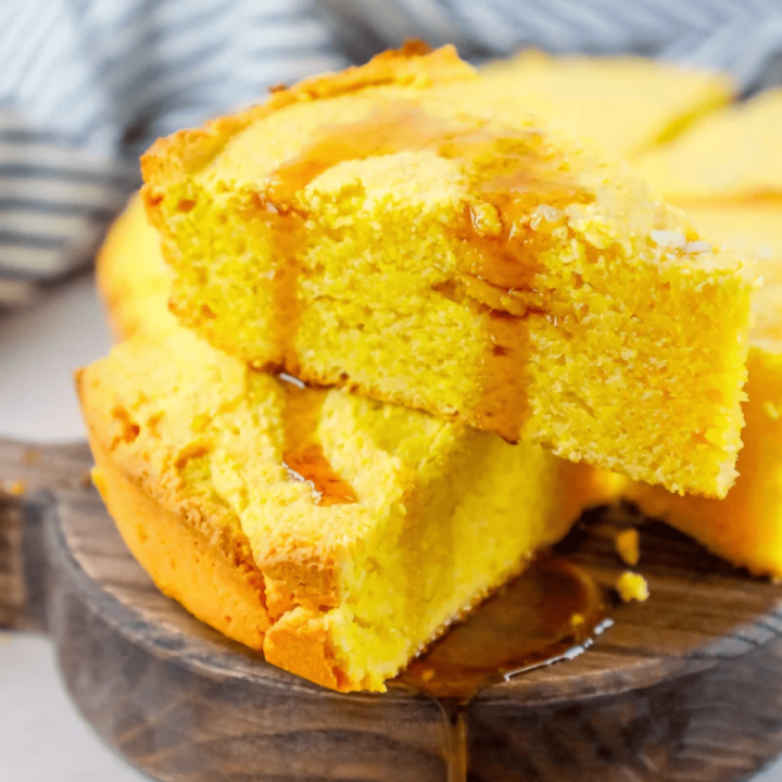 A slice of cornbread on a wooden plate, made with the best cornbread recipe ever.