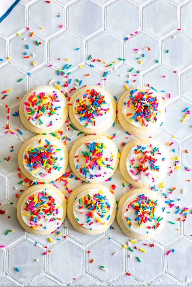 picture of 9 sugar cookies covered in sprinkles with sprinkles all over table