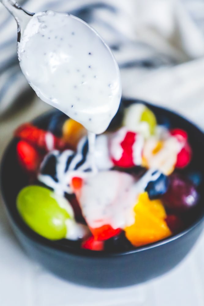 A lemon poppyseed glazed spoon is drizzling over a bowl of fruit salad.