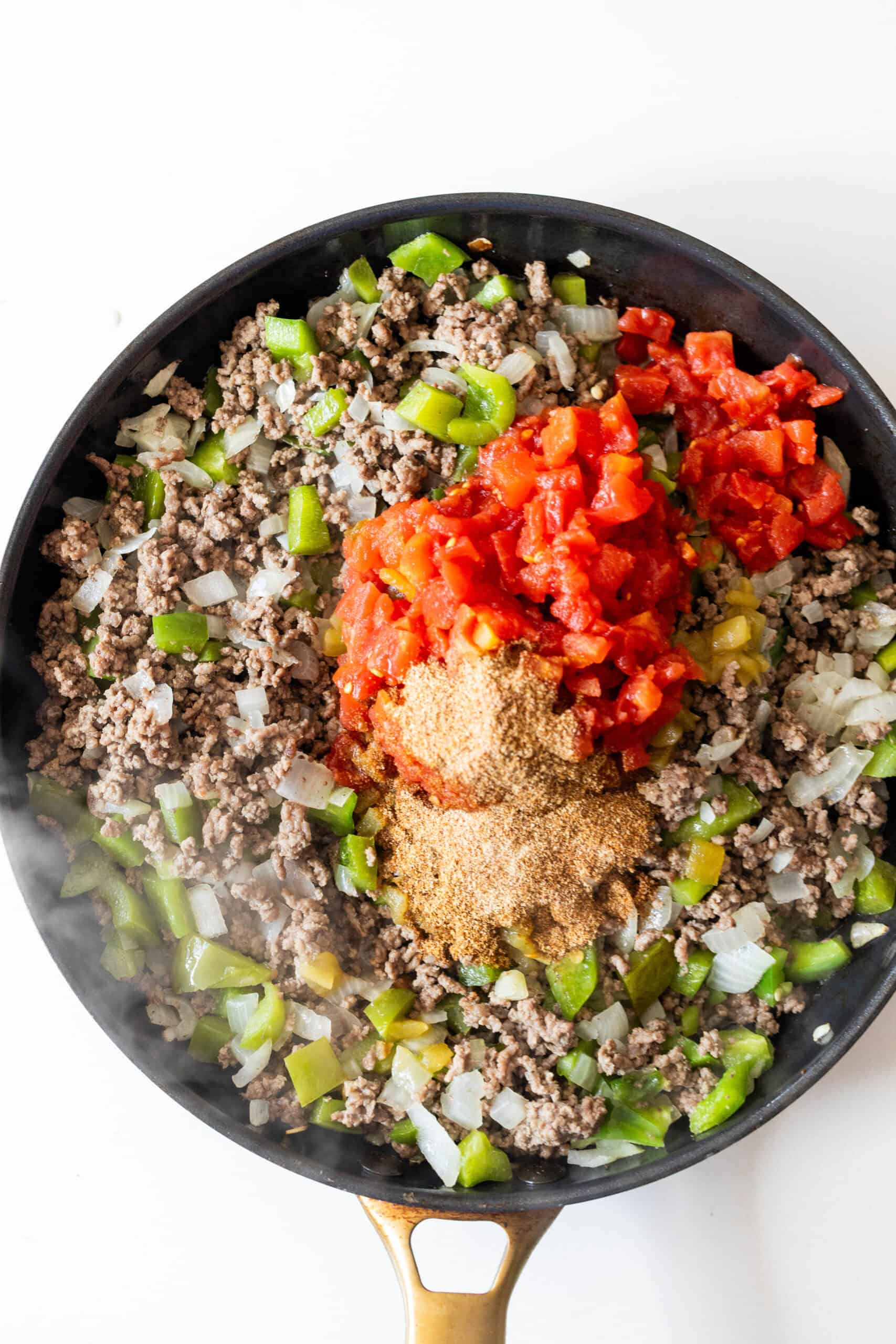 A skillet filled with cooked ground beef, chopped green bell peppers, onions, canned diced tomatoes, taco seasoning, and rice makes this One Pot Spicy Taco Rice Skillet a flavorful dinner option.