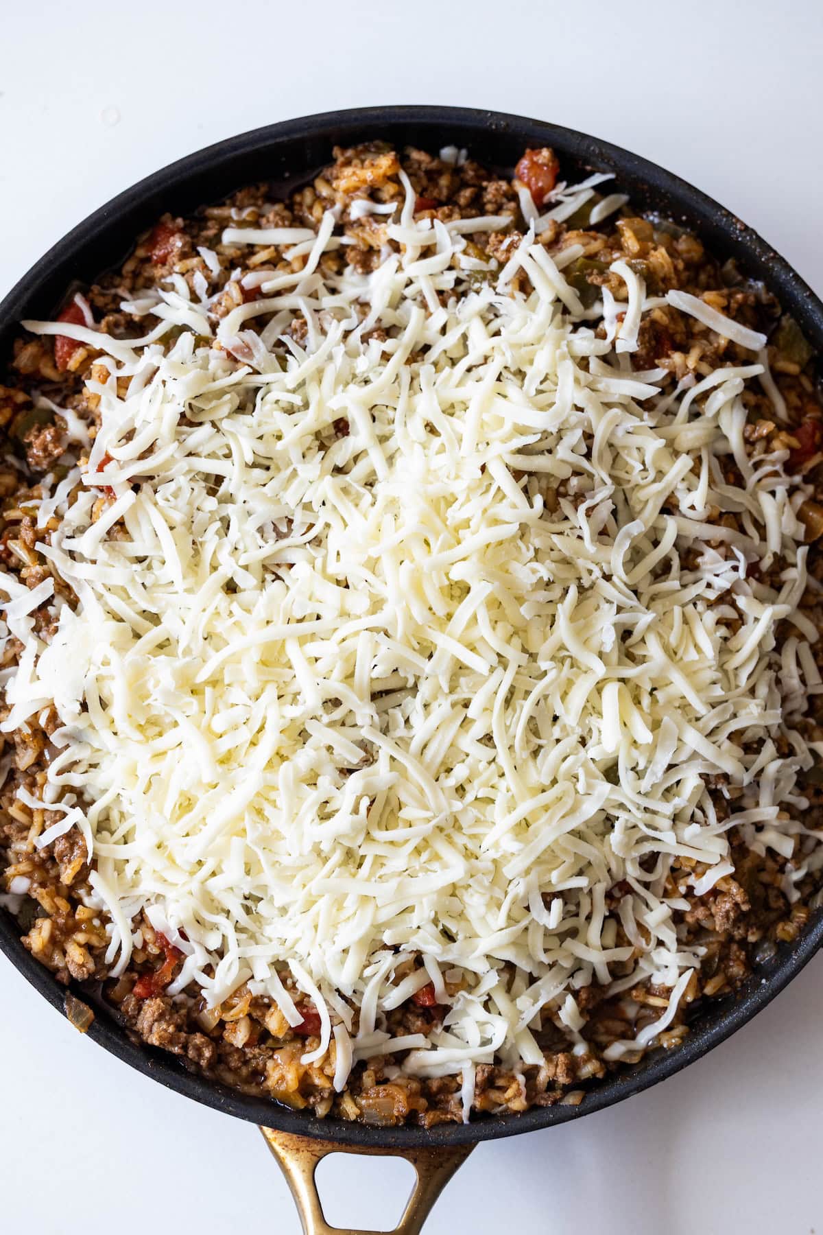 A skillet filled with a ground meat and vegetable mixture, topped with shredded cheese, makes this One Pot Spicy Taco Rice Skillet an easy taco and rice skillet dinner, perfect for cooking or baking.
