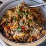 A bowl of cheesy ground beef and rice casserole, reminiscent of an easy taco and rice skillet dinner, topped with chopped parsley and served with a fork.