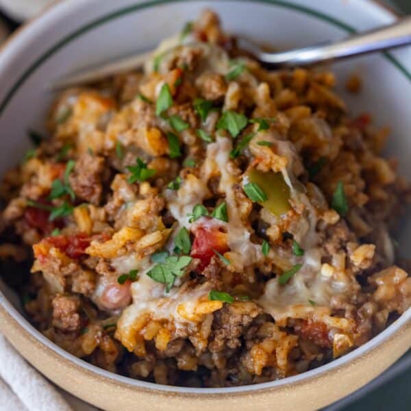 A bowl of cheesy ground beef and rice casserole, reminiscent of an easy taco and rice skillet dinner, topped with chopped parsley and served with a fork.