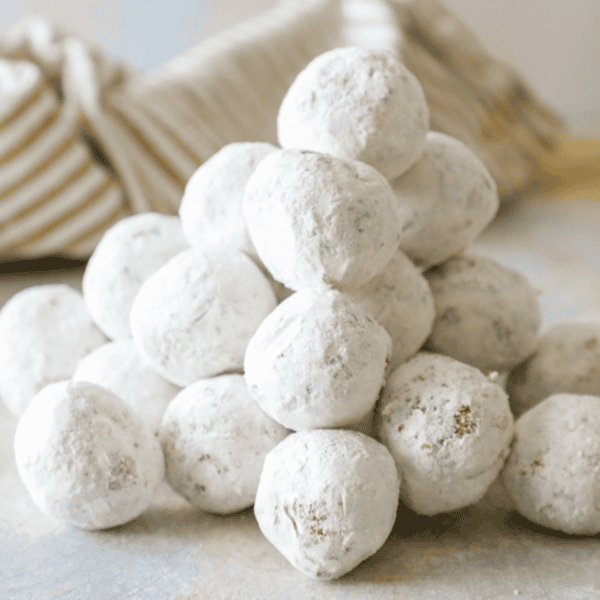 A pyramid of powdered sugar donut holes stacked on a light-colored surface, with a striped cloth in the background.