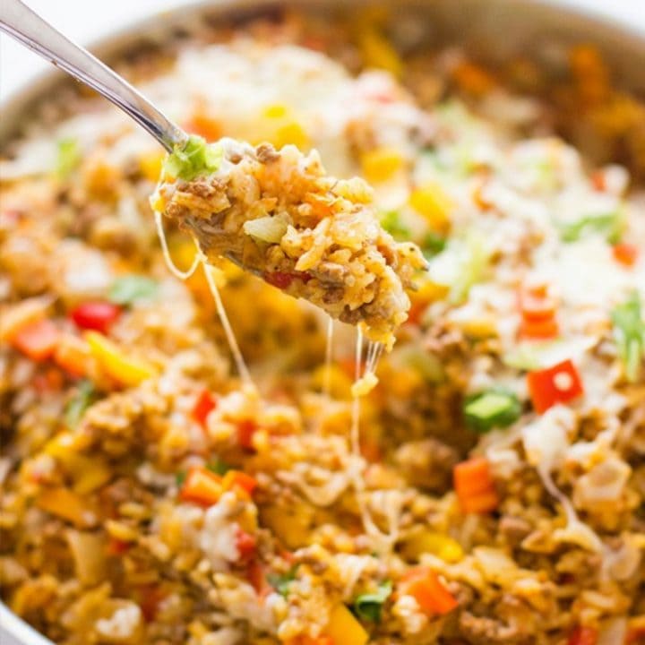 A spoon is being lifted out of a One Pot Spicy Taco Rice Skillet.