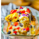 A fork lifts a portion of cheesy chicken taquito casserole topped with melted cheese, diced tomatoes, red onions, cucumbers, and black olives from a glass baking dish.