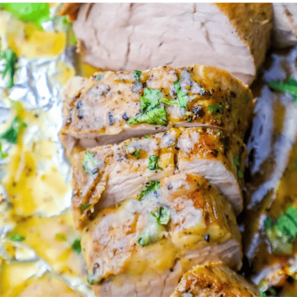 Sliced Baked Ranch Pork Tenderloin topped with herbs and black pepper, resting on a foil-lined surface with savory sauce.