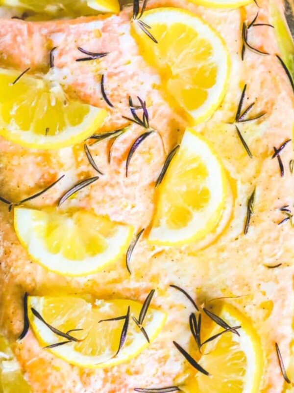 baked salmon filet on a baking sheet lined with foil topped with butter, rosemary, and lemon slices