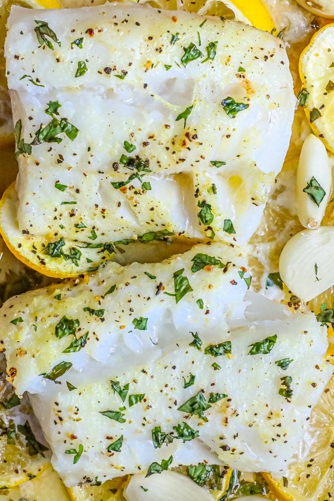 picture of baked cod in a ceramic dish with lemon slices and garlic cloves in the dish 