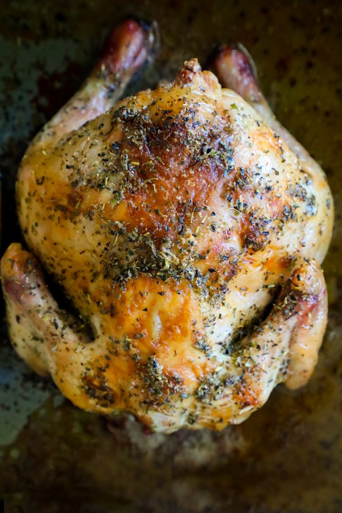 Roasted cornish game hen on a baking sheet with herbs and butter
