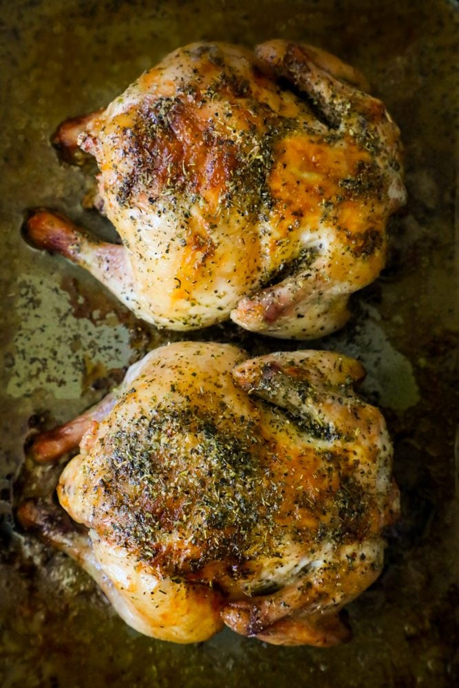 picture of two cornish game hens on a baking sheet with herbs