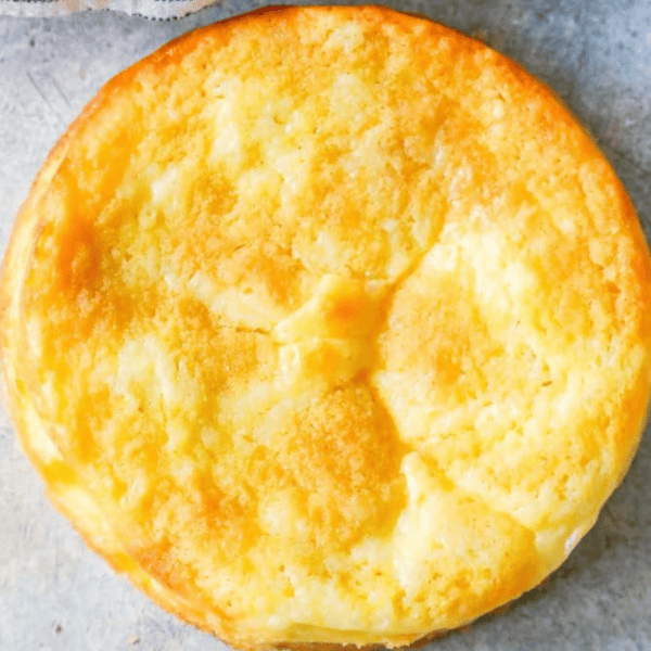 Close-up view of a golden-brown baked cheese soufflé, an easy keto cake, on a light gray surface.