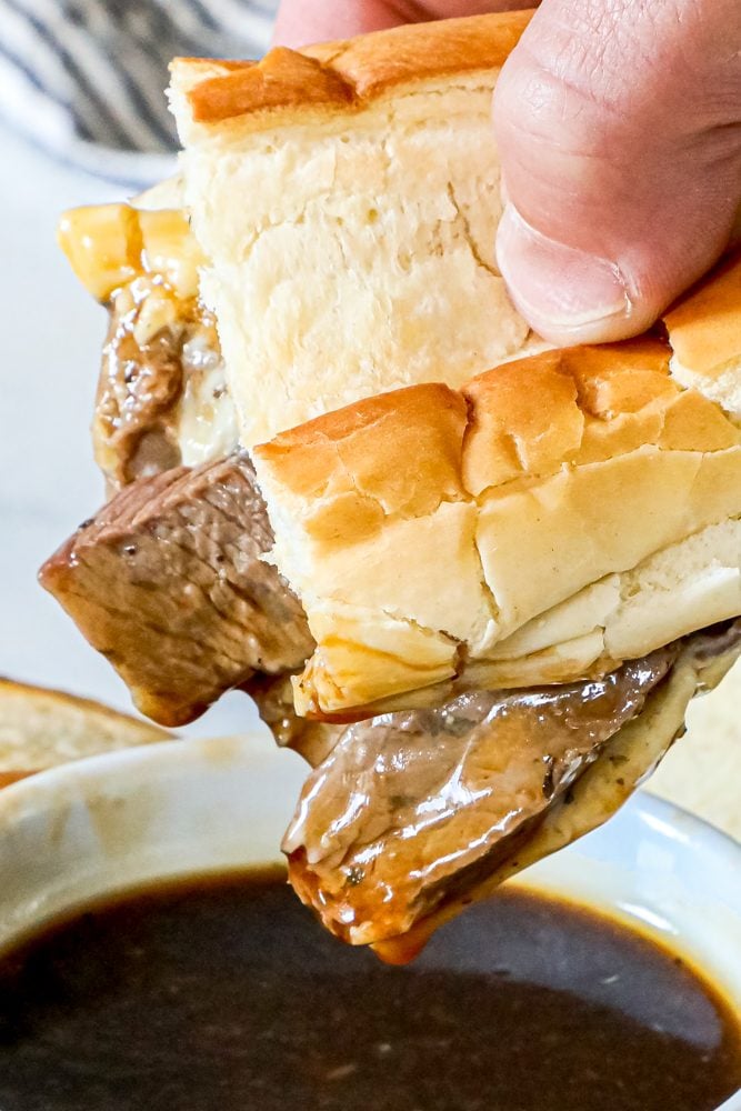 picture of french dip sandwich being dipped into au jus 