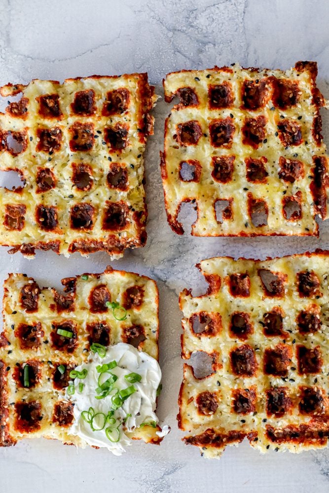 4 keto chaffle waffles on a countertop with sour cream and green onions on one of them.