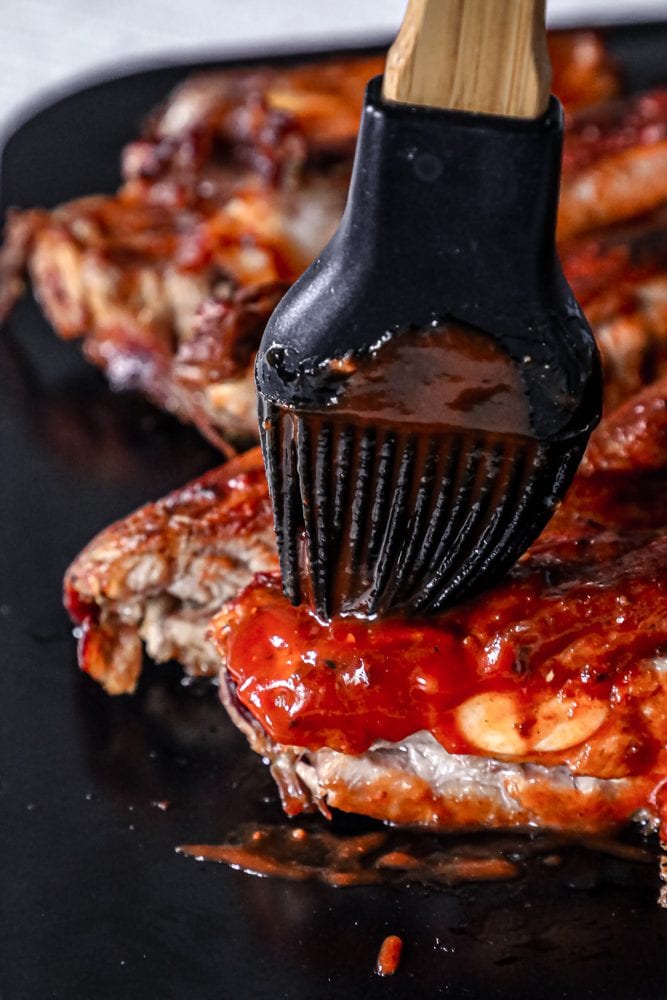ribs covered in barbeque sauce being spread on with brush