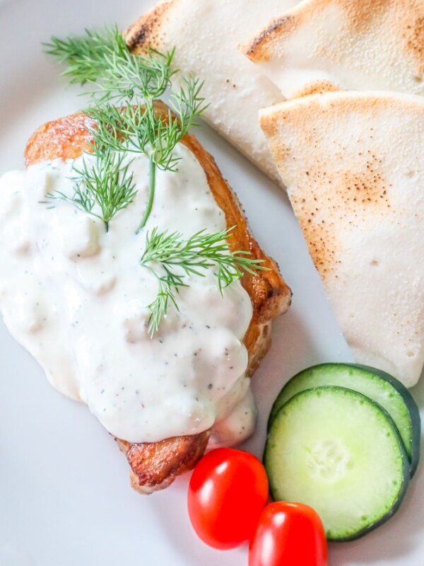 A plate with chicken, tomatoes, and cucumbers served with a creamy feta sauce.