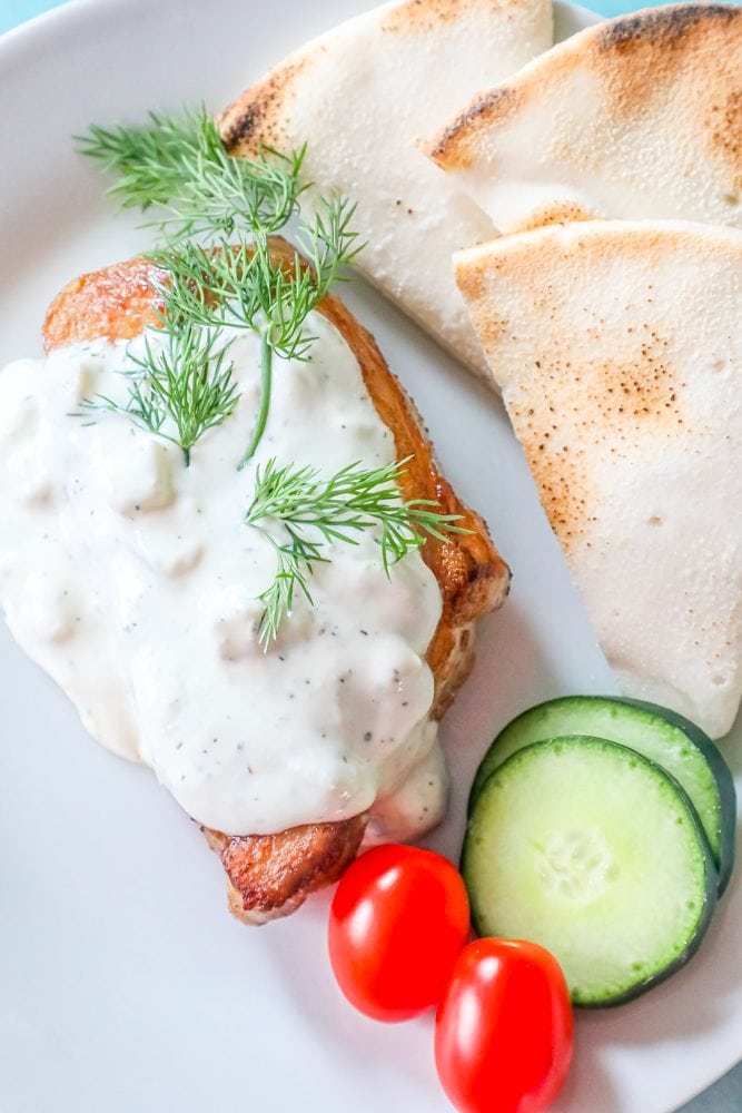 picture of pork chop in feta sauce with cucumbers and tomatoes on a plate
