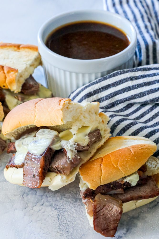French dip sandwiches with melted cheese in front of au jus dip picture