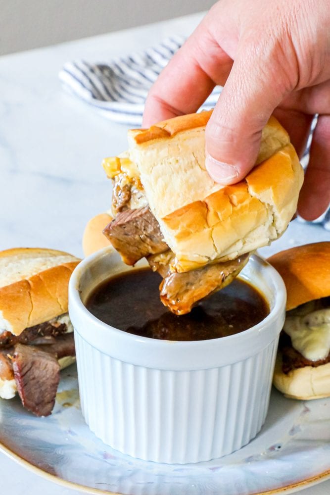 Photo of hand dipping french dip sandwich into pot of au jus sauce