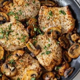 Pan-seared pork chops with sautéed mushrooms, garnished with chopped parsley, in a skillet—just like the best garlic butter pork chops, all made in one pot for easy cleanup.