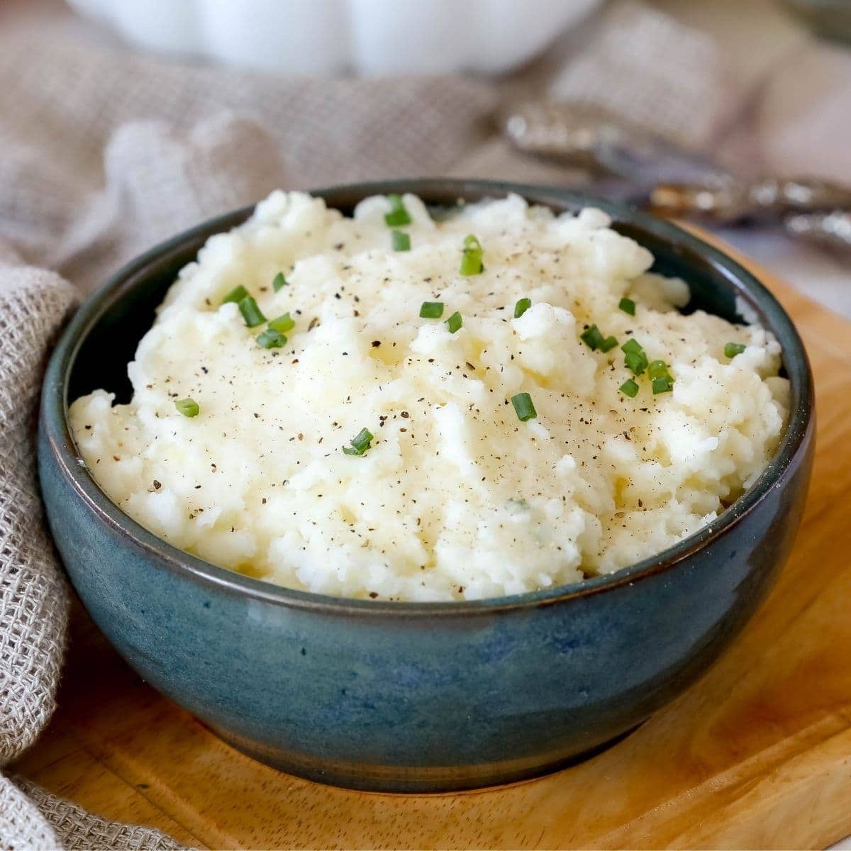 A bowl of creamy mashed potatoes on a cutting board.