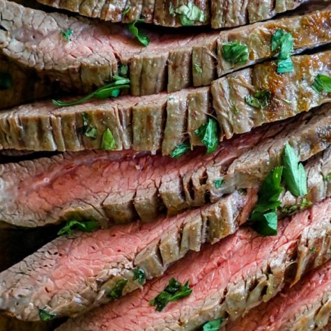 Steak with herbs on a cutting board prepared with a garlic butter roasted flank steak recipe.