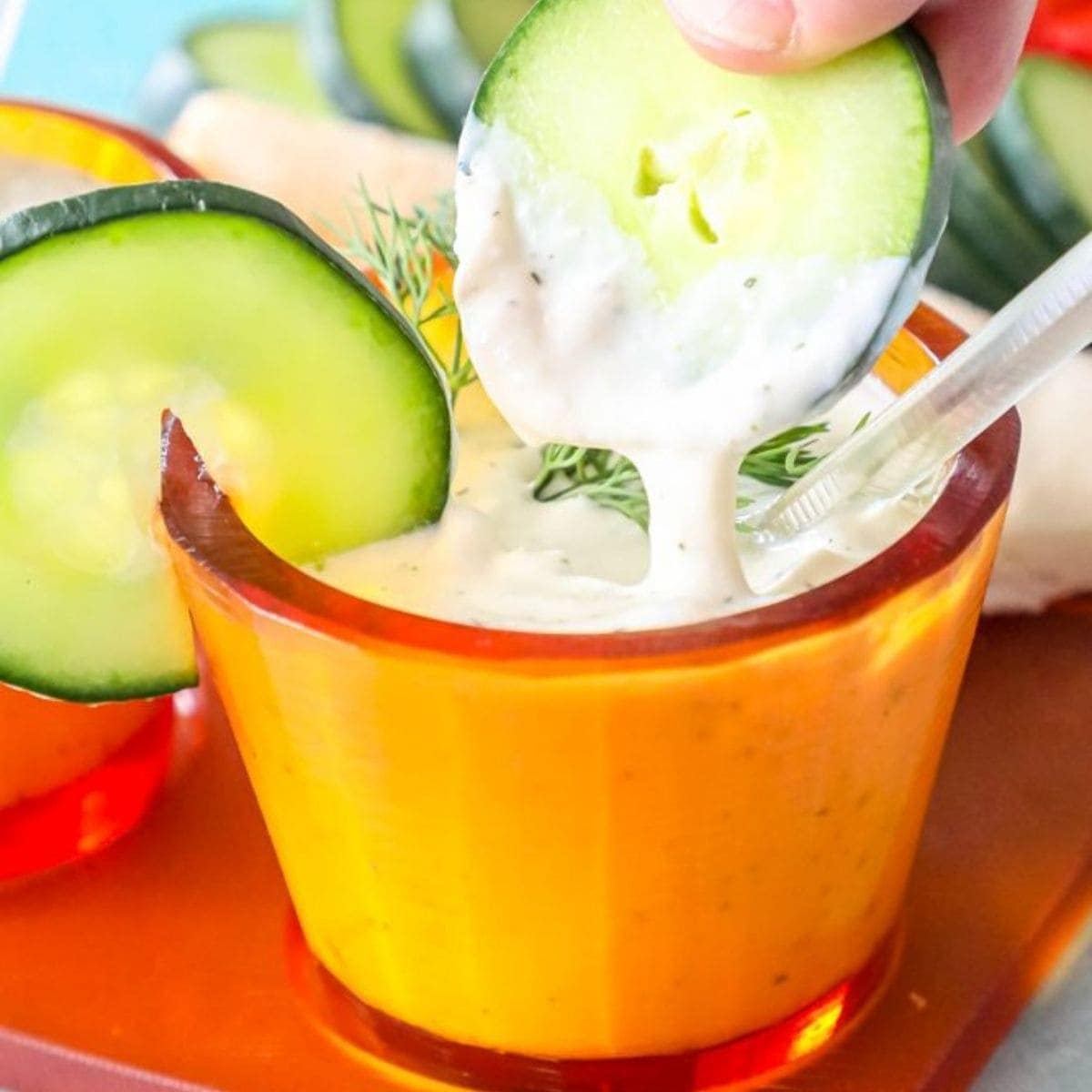 a slice of cucumber being dipped into tzatziki sauce in an orange cup