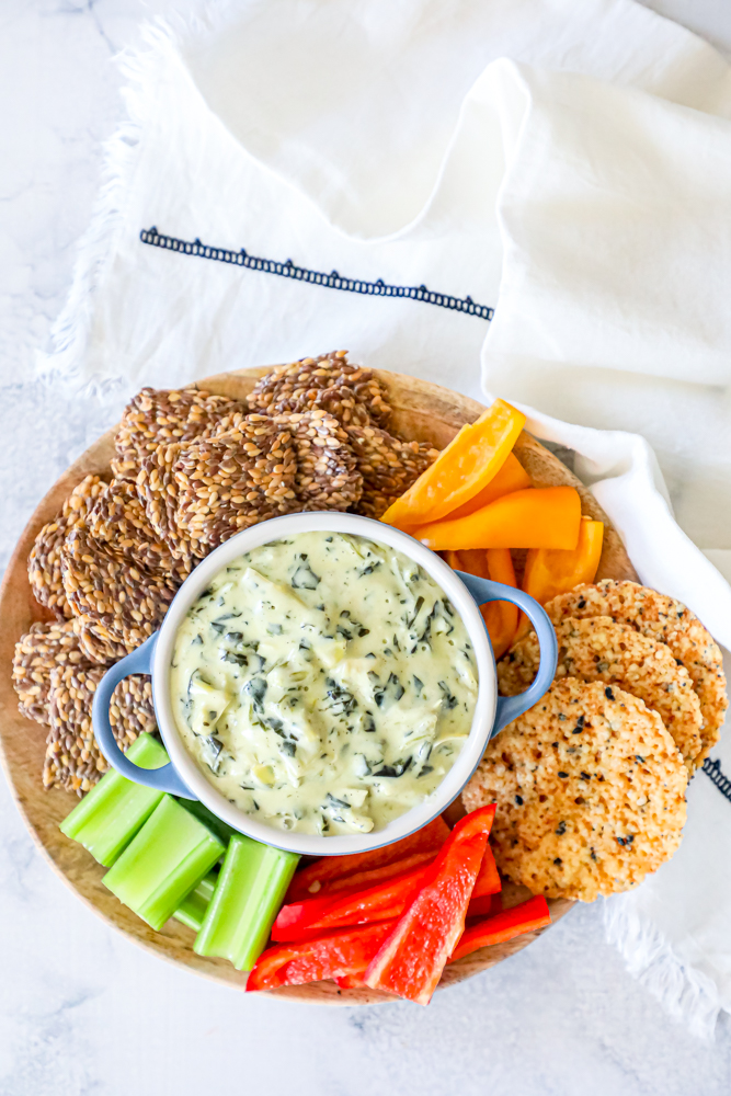 spinach dip in a center bowl with crackers, peppers, and celery around it
