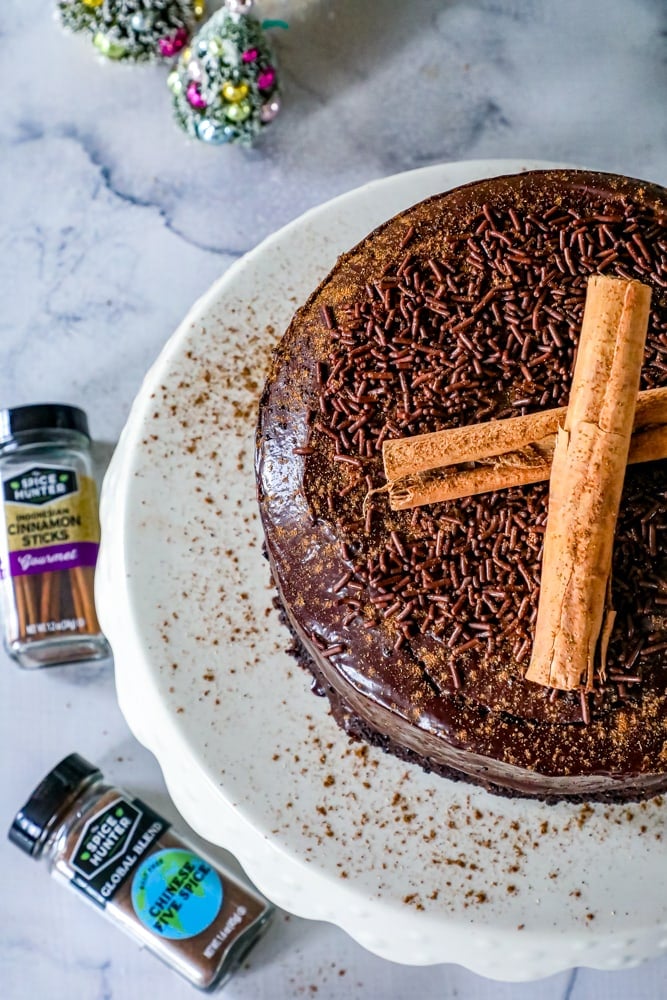 chocolate cake with sprinkles and cinnamon sticks on it and Chinese five spice in a jar.