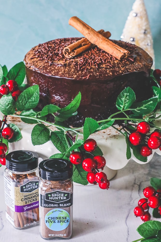 chocolate cake with cinammon sticks on it and holly around it and spices around it. 